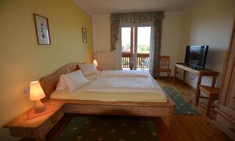 A cozy bedroom with a large wooden double bed. There is a TV, a table and chairs, as well as a balcony with a view.