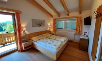 A bright bedroom with wooden ceilings and a cozy double bed. Large windows offer a beautiful view of nature.