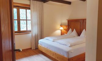 A cozy bedroom with a large double bed and wooden details. The window lets in plenty of daylight and gives the room an inviting atmosphere.