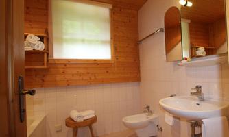 A modern bathroom with wooden paneling, a bathtub, and a sink. Clean towels are ready, and the light is friendly and inviting.