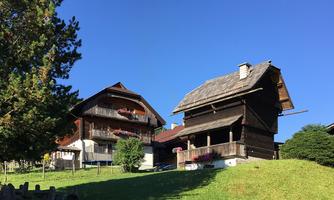 View of two traditional wooden houses in a green landscape. The sky is clear and blue.