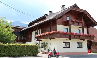A traditional, charming wooden house with flower boxes on the balconies. The surroundings are green and well-maintained, ideal for a cozy home.