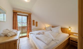 A cozy bedroom with wood paneling and plenty of natural light. The room features a large bed and a balcony with a view.