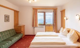 A cozy hotel room with two beds and a sofa bed. Large windows offer a view of the landscape.