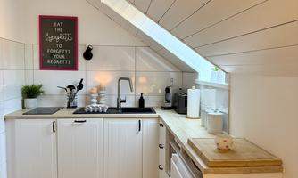 A modern kitchen with white cabinets and wood details. A window lets in a lot of light and there is an inspiring wall decoration.
