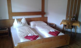 A simple and modern bedroom with two single beds. There is a small table and chairs, as well as a warm wooden tone in the decor.