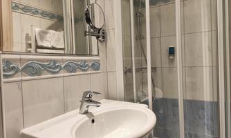 A small bathroom with a sink and a shower cubicle. The walls are tiled and decorated in light colors.