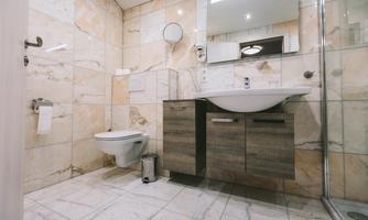 A modern bathroom with stylish tiles and wooden details. It includes a sink, a shower, and a toilet.
