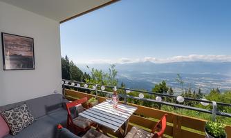 A cozy balcony with a view of the mountains and the valley. The table is set, and there is a relaxing atmosphere.