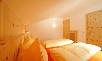 A cozy bedroom with wooden walls and large pillows. Light gently streams through the room, creating a relaxed atmosphere.