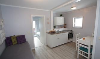 A modern kitchen with a dining area and a cozy sofa. The room is bright and inviting, with neutral colors and a clear structure.