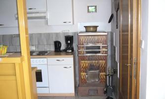 A modern kitchen with white cabinets and an old wood stove. On the countertop are a coffee pot and a fruit bowl.
