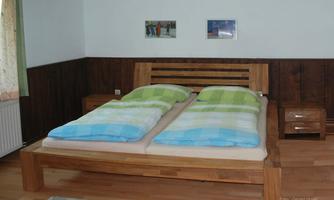A cozy bedroom with a large double bed and beige fast-drying bedspreads. Two pictures are hanging on the wall, and the room has wood-paneled walls.