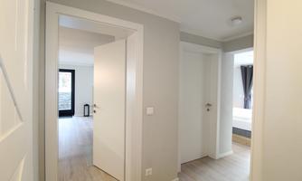 A bright hallway with several closed doors. The walls are in a neutral gray tone and the floor is light.