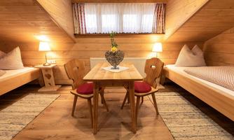 A cozy room with wooden walls and two single beds. A table with a flower vase and two chairs creates an inviting atmosphere.