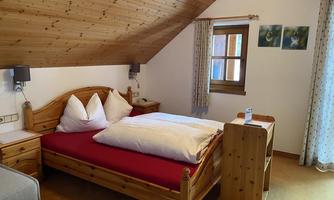 A cozy bedroom with a wooden bed and red bedding. The walls are adorned with wood paneling and windows dressed with curtains.