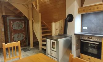 A cozy kitchen with a wood stove and modern stove. In the background, a staircase and a traditional cabinet are visible.