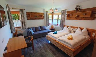 A cozy room with a double bed and a sofa bed. Wooden shelves and windows create a warm, inviting atmosphere.