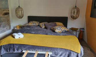 A cozy bedroom with a large bed and colorful pillows. The walls are painted in warm colors, and stylish lamps hang over the bed.