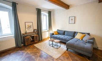 A stylish living space with a gray sofa and colorful cushions. Next to a window stands a small table on a light carpet.