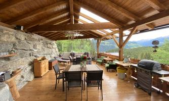 A cozy porch with a wooden floor and a rustic roof. There is a dining area and comfortable seating with a view of the mountains.