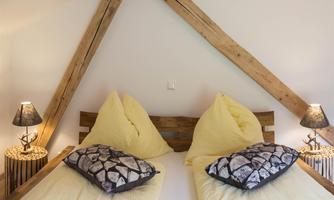 A cozy bedroom with two single beds and yellow blankets.  
Wooden beams and stylish nightstands give the room a warm atmosphere.