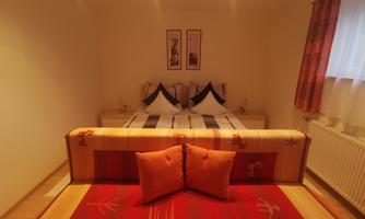 A cozy room with a large bed and a colorful couch. The room has bright walls and plenty of natural light.