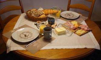 A laid breakfast table with various rolls, cold cuts, cheese, and drinks. The atmosphere is cozy and inviting.