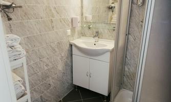 A small bathroom with modern tiles and a sink. The shower is separated and towels are neatly stacked.