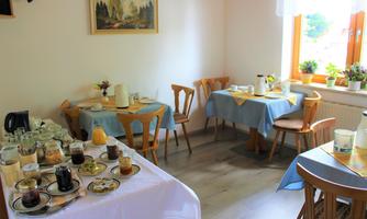 An inviting breakfast room with set tables. There are various foods and drinks as well as a bright, friendly atmosphere.