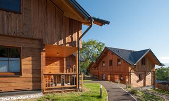 Two modern wooden houses in a quiet setting. A paved path leads through the green grass between the buildings.