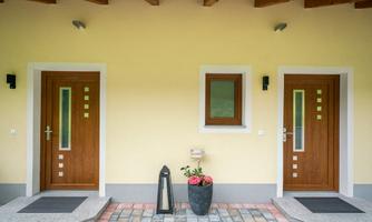 Two entrances with wooden doors on a yellow wall. In front of the doors, there is a flowerpot with flowers.