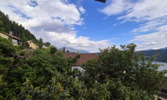 A picturesque landscape with green trees and a clear sky. In the background, there are hills and a lake.
