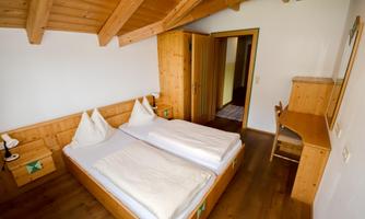 A cozy room with two single beds and wooden paneling. There is a desk and access to another room.