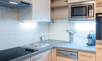 A modern kitchen with a sink, a stove, and a microwave. The furnishings are minimalist and well-organized.