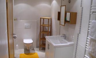 A modern bathroom with bright tiles and a shower. A wooden shelf, sink, and toilet area are well arranged.