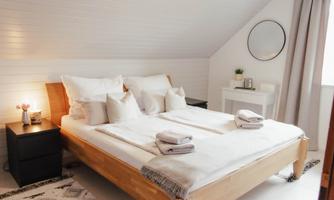 A cozy bedroom with a large bed and white bedding. There is a bedside table and a mirror on the wall.