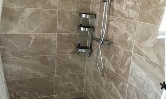 A modern shower with tiled walls and a sleek showerhead. The floor is also tiled and appears well-maintained.