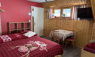 A cozy room with two beds and rustic wood design.  
There are chairs by the table and a window with fresh flowers.