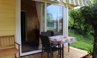 A cozy balcony with a small table and two chairs. In the background, there are green trees and a pleasant atmosphere.