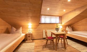 A cozy room with wooden walls and two single beds. There is a table with chairs and warm light from the lamps.