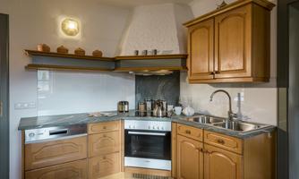 A modern kitchen with wood cabinets and a stone countertop. The kitchen is well equipped with a stove, a refrigerator, and a sink.