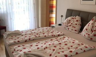 A cozy bedroom with a double bed and bedding in floral patterns. Bright light falls into the room through the window.