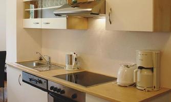 A modern kitchen with bright furniture and elegant appliances. The space is functional and well-equipped with a stove, sink, and coffee machine.