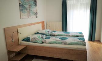 A cozy bedroom with a double bed and colorful bedspreads. The large windows let in plenty of light, and the curtains are in calm colors.
