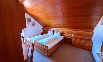 A cozy bedroom with wooden walls and a slanted roof. It is furnished with a double bed and a small table.