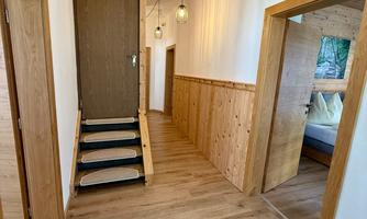 A bright hallway with wood paneling and a staircase. Modern lamps hang on the wall, providing good lighting for the space.