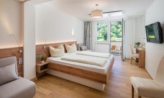 A modern room with two beds and wooden details. Large windows offer a view of nature and provide plenty of light.