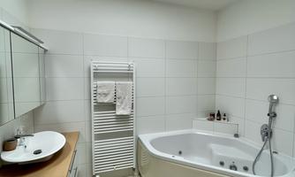 A modern bathroom with a bathtub and a washbasin. It has bright walls and plenty of daylight through the roof window.