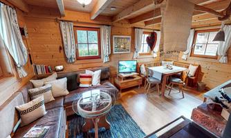 A cozy wooden cottage with an inviting living room. There is a sofa, a dining table, and large windows that let in a lot of light.